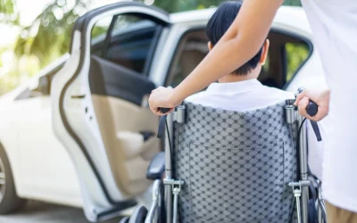 Caregiver helping senior handicapped asian woman from wheelchair get into car